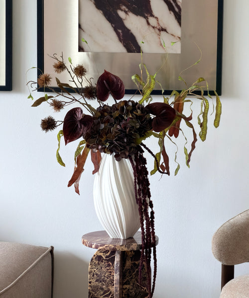 Kunstblumenstrauß Copper Dusk in Bordeaux, Grün & Kupfer aus der Serie Bloom – auf dem Marmorsockel im Wohnzimmer